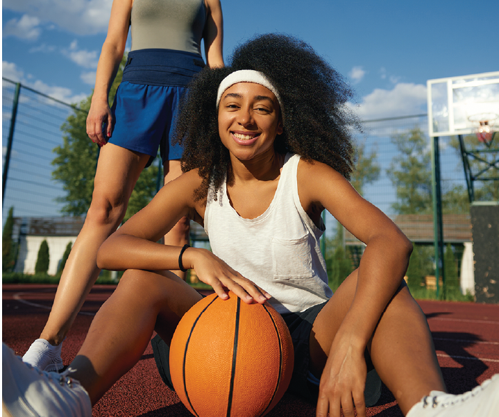 Teenage girl sitting on an outdoor basketball court with a basketball