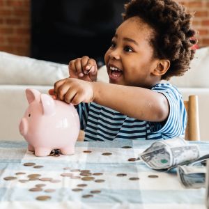 Young child putting coins in a piggy bank.
